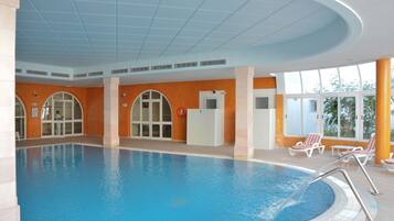 Una piscina interior con agua cristalina, rodeada de paredes naranjas y columnas blancas.