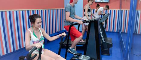 A gym with treadmills and stationary bikes, striped walls, and a television displaying fitness content.