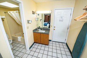 A bathroom with a shower, toilet, sink, and a door with a mirror. - River Place Inn (Pigeon Forge)