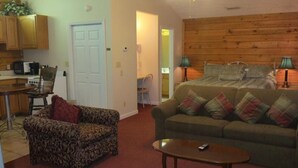 A cozy room with a wooden ceiling, a bed with pillows, a sofa with cushions, a small table, and a chair. - River Place Inn (Pigeon Forge)