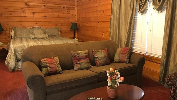 A cozy room with a wooden interior, a bed with a patterned bedspread, a sofa with plaid cushions, and a small table with a vase of flowers. - River Place Inn (Pigeon Forge)