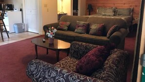 A cozy living room with a sofa, armchair, and a coffee table. A bed with pillows is visible in the background. - River Place Inn (Pigeon Forge)