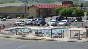 Um hotel com piscina, vários espaços de estacionamento e um edifício com telhado vermelho ao fundo.