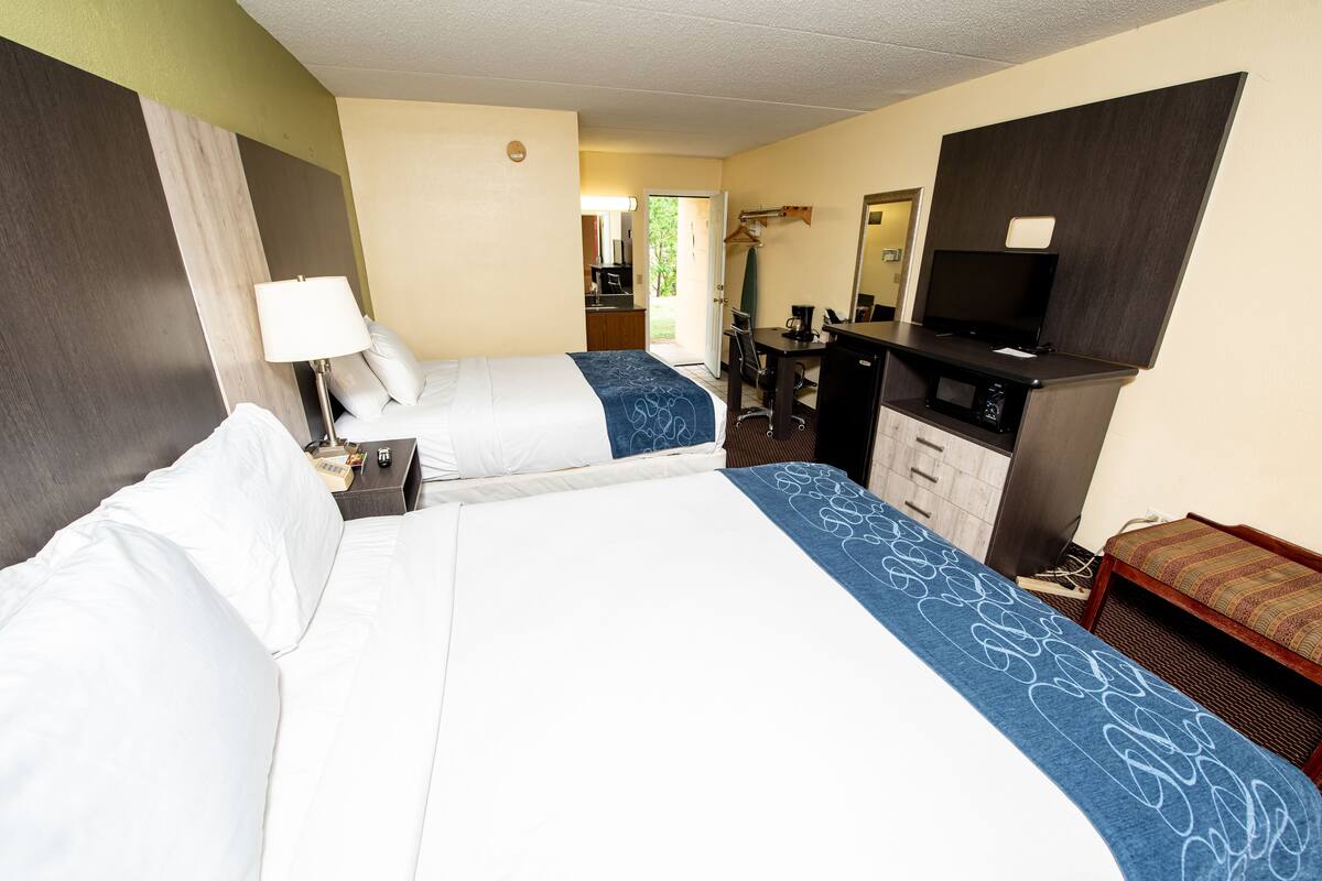 A hotel room with two beds, a desk, a microwave, and a TV.