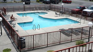 A rectangular outdoor swimming pool with a red metal fence, multiple lounge chairs, and a small table. - River Place Inn (Pigeon Forge)