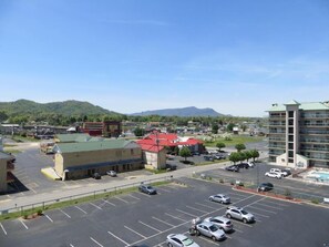 A parking lot with multiple cars, a building with a red roof, and a mountain in the background. - River Place Inn (Pigeon Forge)