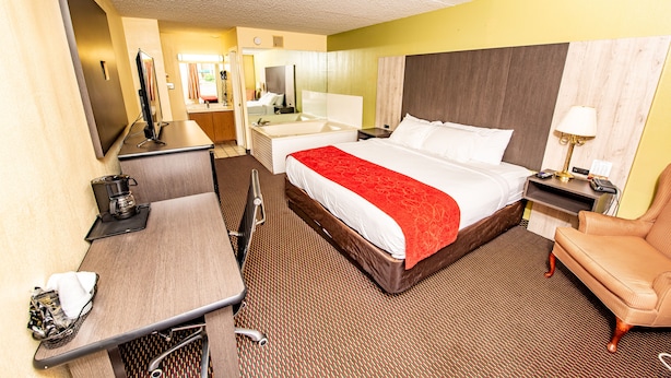 A hotel room with a large bed, a desk, a chair, a TV, a mirror, and a bathroom. - River Place Inn (Pigeon Forge)