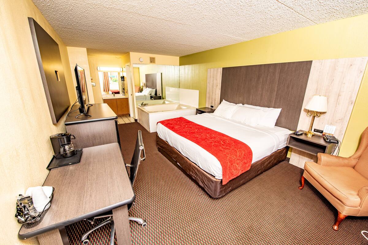A hotel room with a large bed, a desk, a chair, a TV, a mirror, and a bathroom.