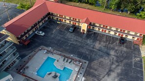 Vista aérea de um hotel com telhado vermelho, piscina e estacionamento.