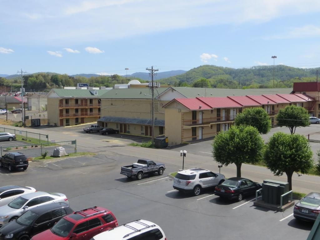 Un parking avec plusieurs voitures, un bâtiment doté d’un toit rouge et un paysage montagneux en arrière-plan.
