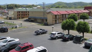 A parking lot with several cars, a building with a red roof, and a mountainous background. - River Place Inn (Pigeon Forge)