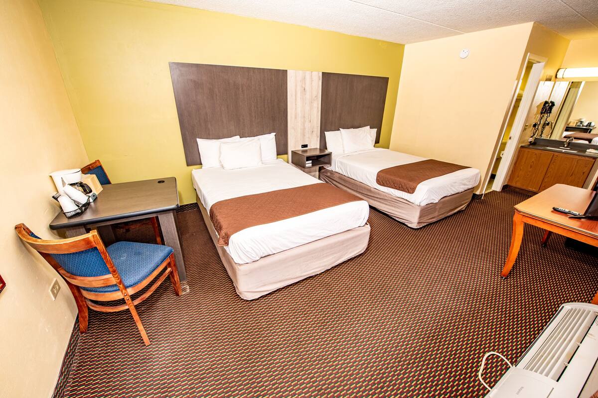 A hotel room with two beds, a desk, a chair, a small table, and a bathroom area.
