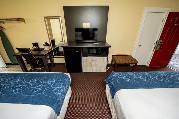 Quarto de hotel com duas camas, uma secretária com um computador, uma televisão e uma porta vermelha.