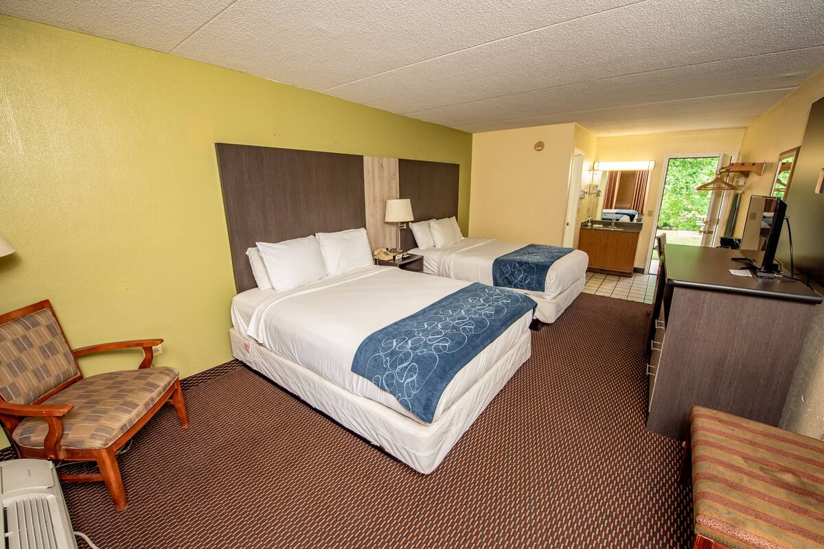 A hotel room with two beds, a desk, a chair, and a bathroom visible through an open door.