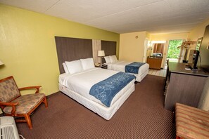 Quarto de hotel com duas camas, uma escrivaninha, uma cadeira e um banheiro visível por uma porta aberta.