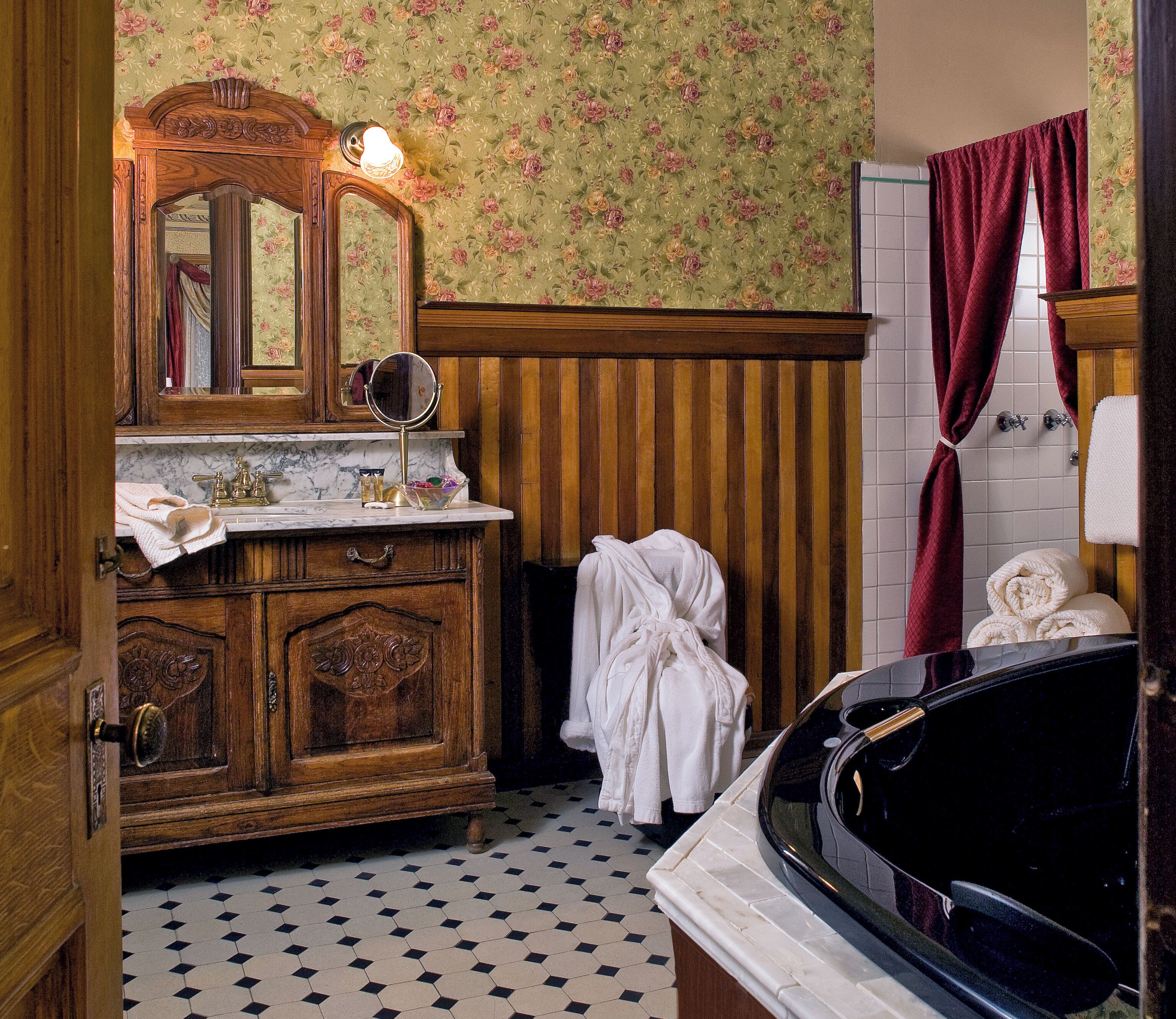 Un baño de estilo vintage con un tocador de madera, un espejo grande, una bañera y un papel tapiz floral.