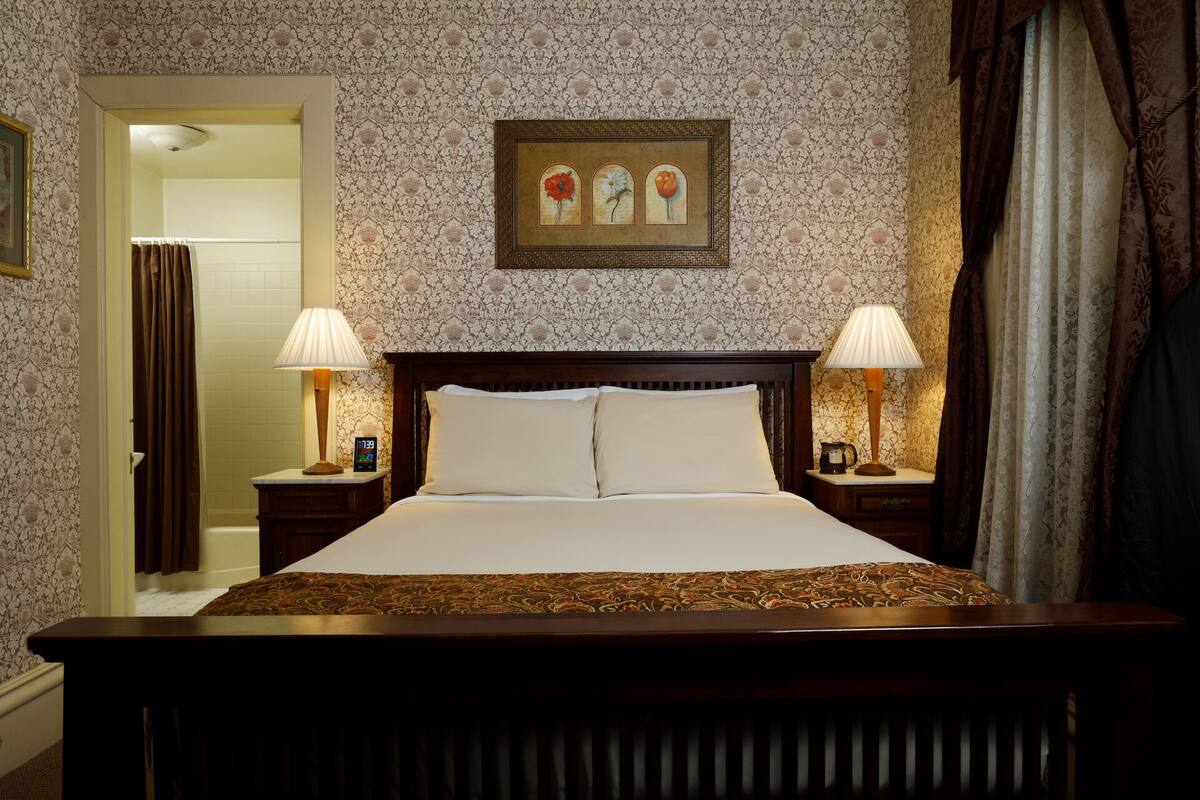 A hotel room with a large bed, two bedside lamps, a clock, and a framed picture on the wall.