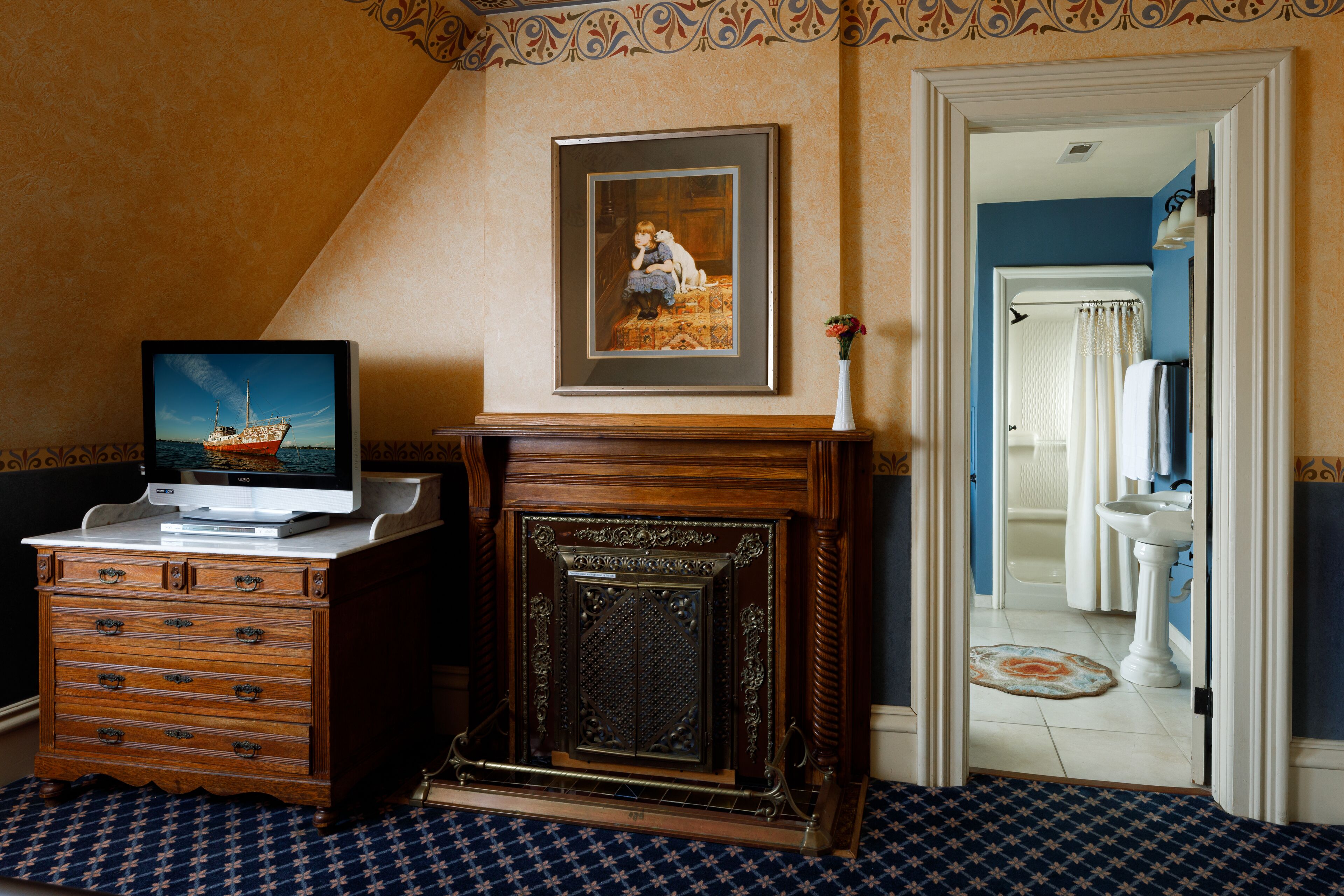 Una habitación con chimenea, un televisor sobre un tocador, y un baño a la vista a través de una puerta abierta.