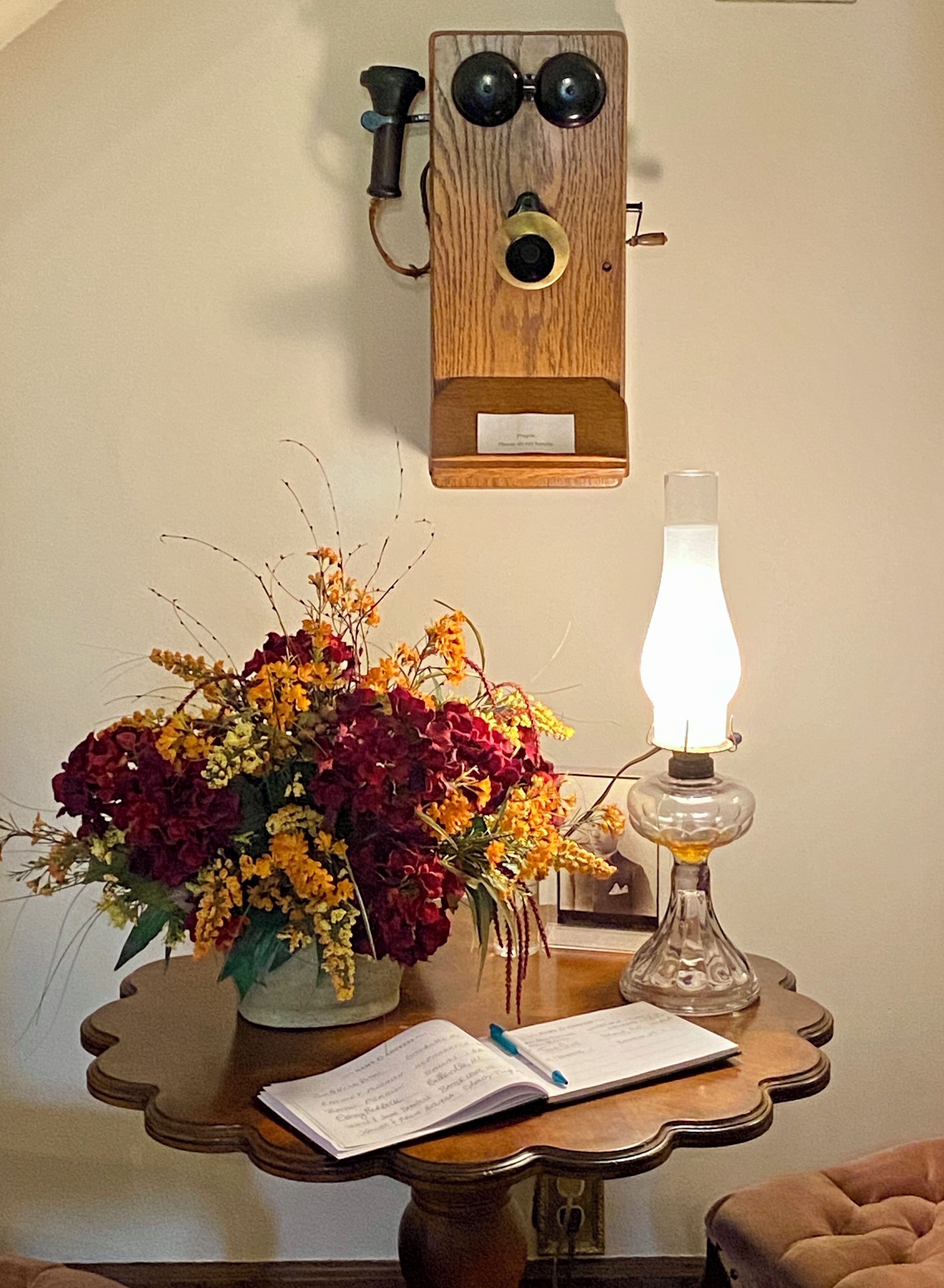 A table with a vase of flowers, a lit lamp, and a notebook.