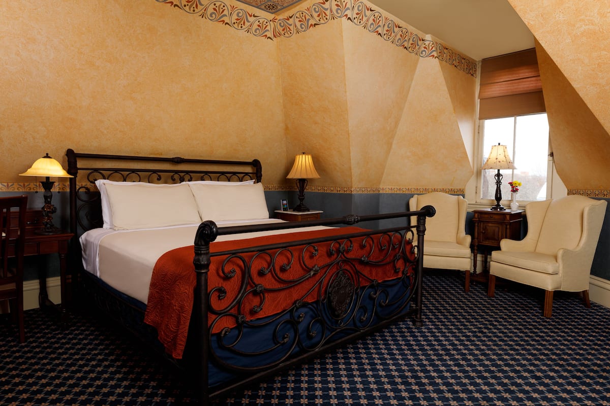 A hotel room with a large bed, two bedside tables with lamps, a chair, and a window with a view.