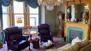 A room with two leather armchairs, a sofa, a chandelier, a fireplace, and a large mirror. - The Kalamazoo House Downtown Hotel & Suites (Kalamazoo)