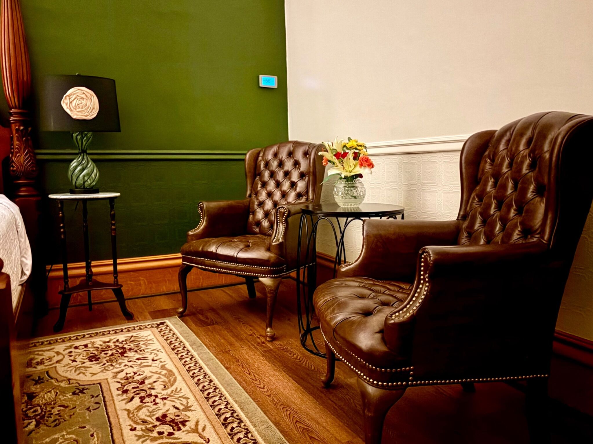 Une pièce avec deux fauteuils en cuir, une petite table sur laquelle est posé un vase de fleurs, une lampe et un mur vert.