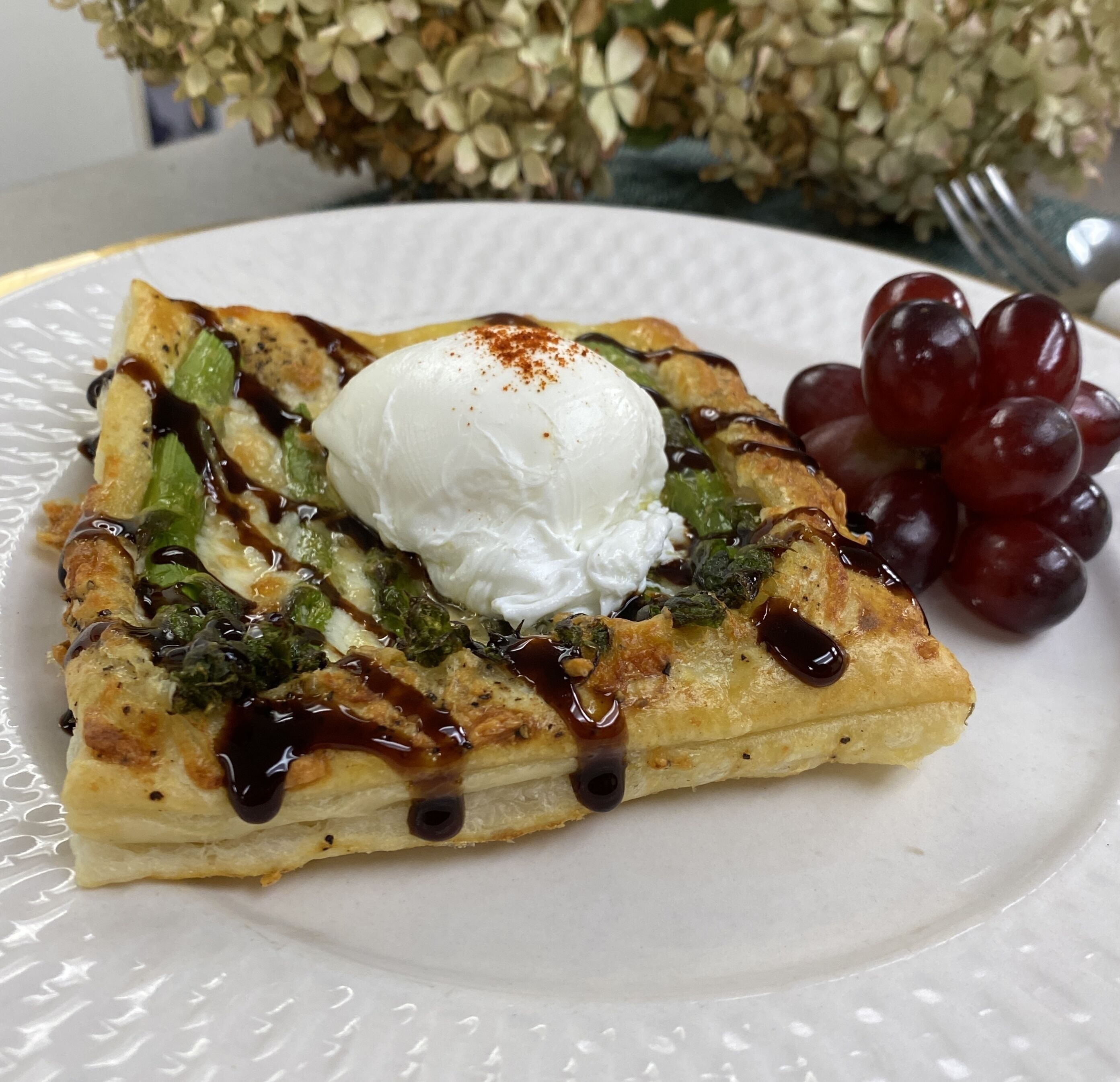 A plate with a savory dish, possibly a quiche or tart, topped with a dollop of cream and drizzled with sauce.