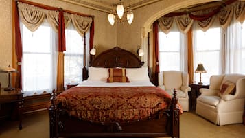 Una cama grande y elaborada con cabecera de madera, flanqueada por dos sillones y una mesita de noche con una lámpara.