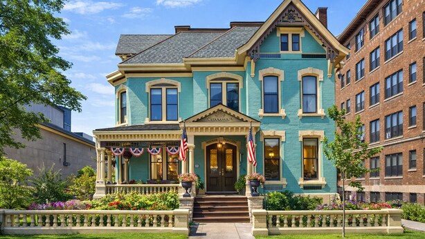 A two-story building with a prominent entrance, a flag, and a well-maintained garden. - The Kalamazoo House Downtown Hotel & Suites (Kalamazoo)