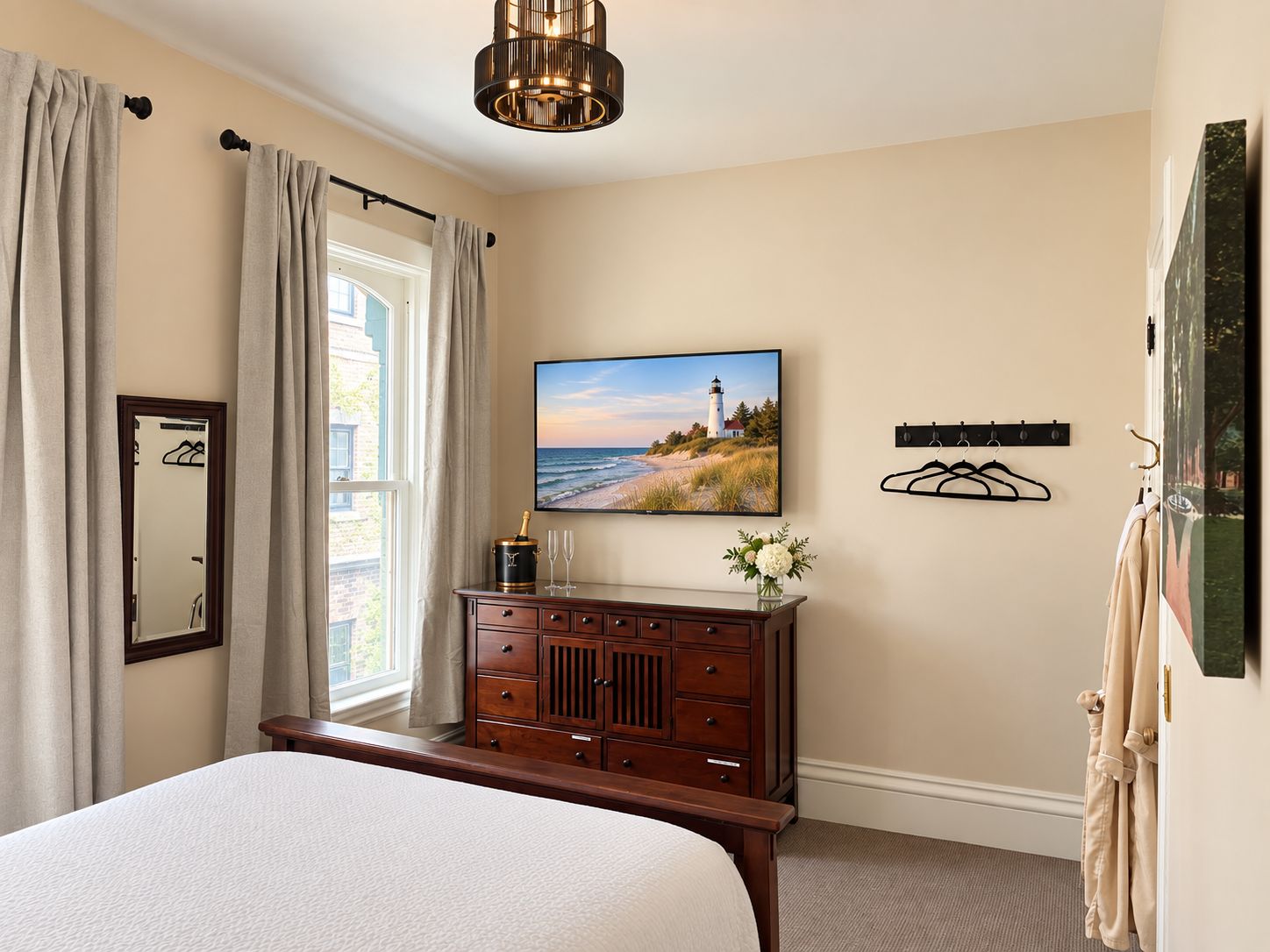 A bedroom with a bed, a dresser, a mirror, a television, and a painting of a lighthouse.
