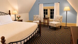 Ein Schlafzimmer mit einem großen Bett, zwei gemusterten Sessel, einem kleinen Tisch mit Wasserkocher und einer Stehlampe.