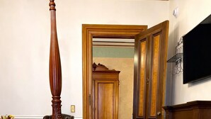 A bedroom with a four-poster bed, a fireplace, a wooden wardrobe, and a carpeted hallway. - The Kalamazoo House Downtown Hotel & Suites (Kalamazoo)