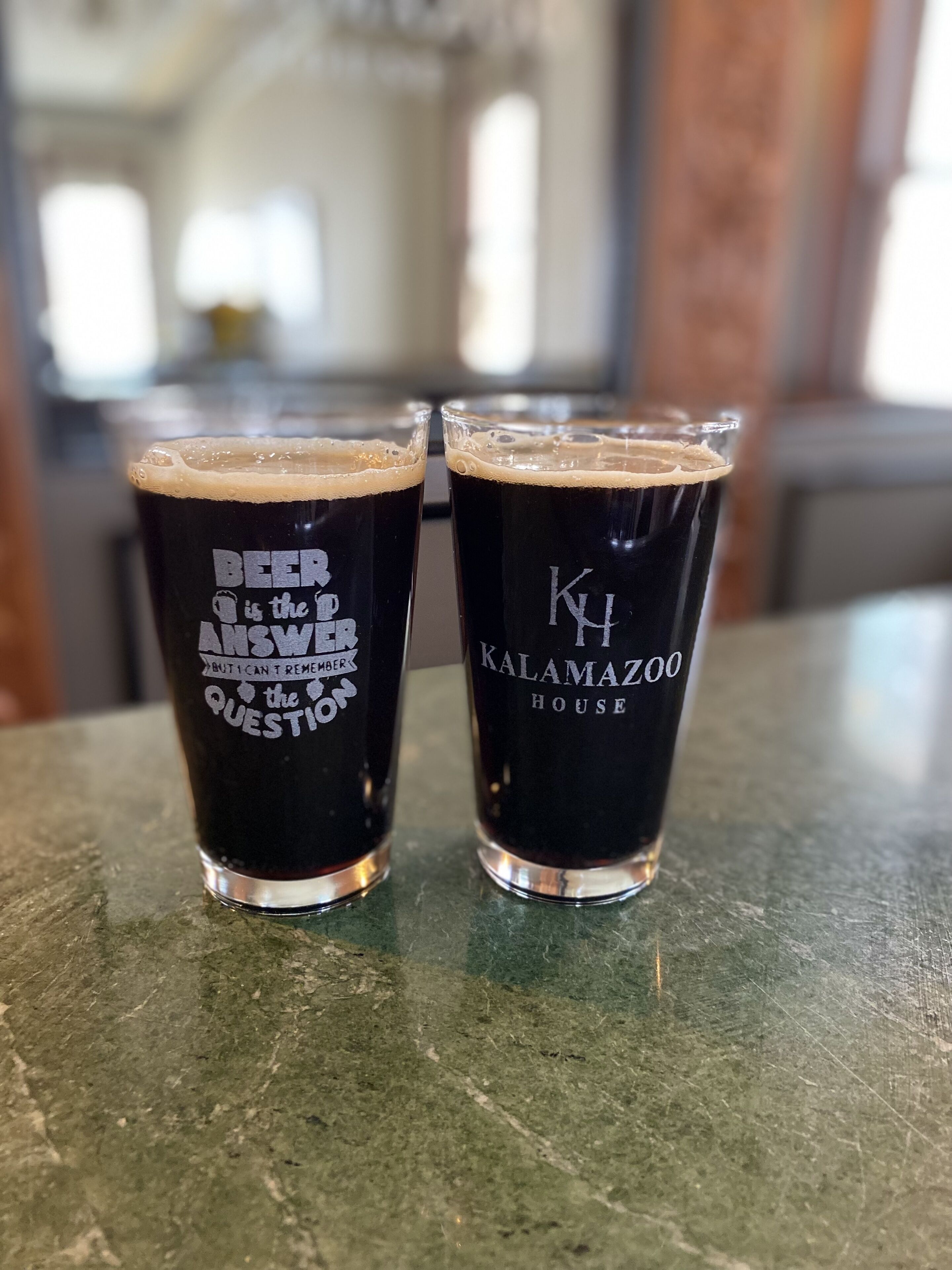 Two glasses of dark beer on a marble countertop.