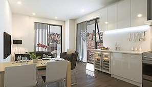Eine moderne Küche mit weißen Schränken, ein Essbereich mit Tisch und Stühlen sowie ein großes Fenster mit Vorhängen.