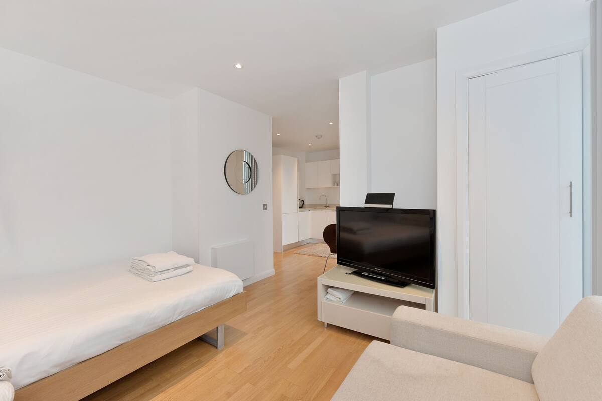 Ein modernes, minimalistisches Zimmer mit Bett, Fernseher auf einem Schrank, einer Couch und einem Kleiderschrank.