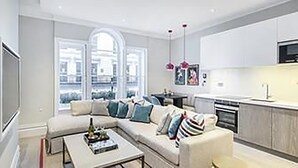 A modern living room with a sectional sofa, a coffee table, and a TV. - The Kensington Residencies (London)