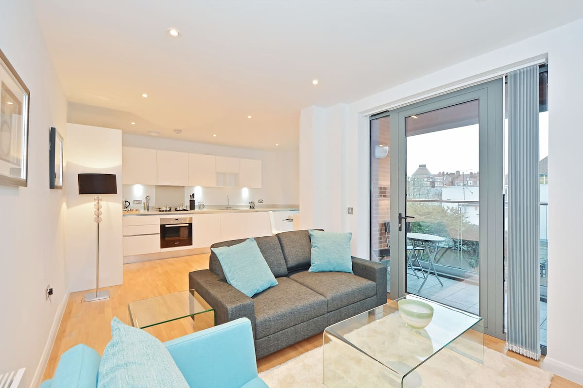Eine moderne Wohnung mit grauem Sofa, einem Glastisch und Blick auf die Stadt durch große Schiebegläser.