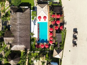 Vista aérea de un resort con piscina, sombrillas rojas y palmeras.