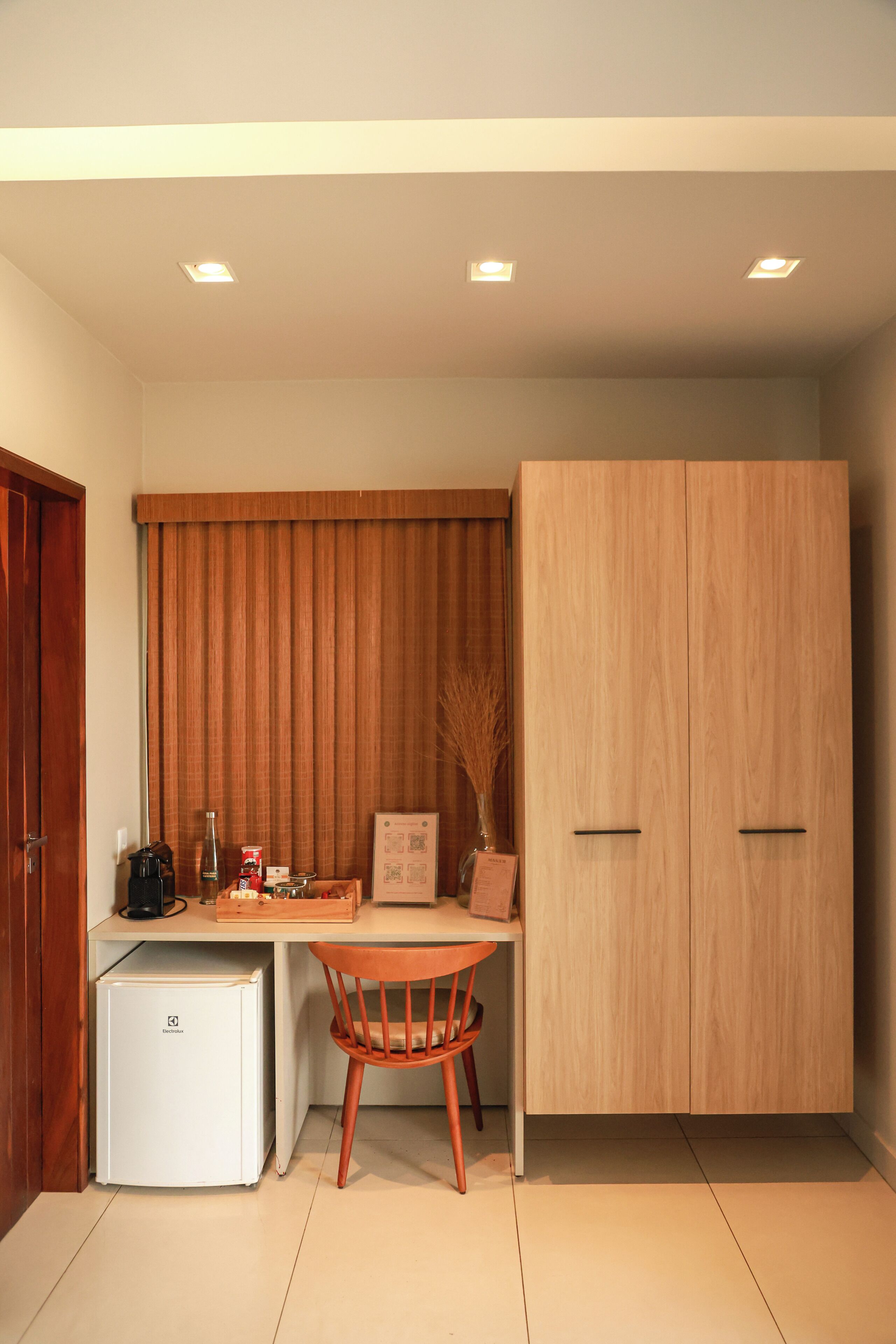 A compact room with a kitchenette, a dining table with a chair, a wardrobe, and a small refrigerator.