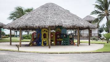 Children can play and explore in this outdoor play area with a thatched-roof structure and colorful play structures.