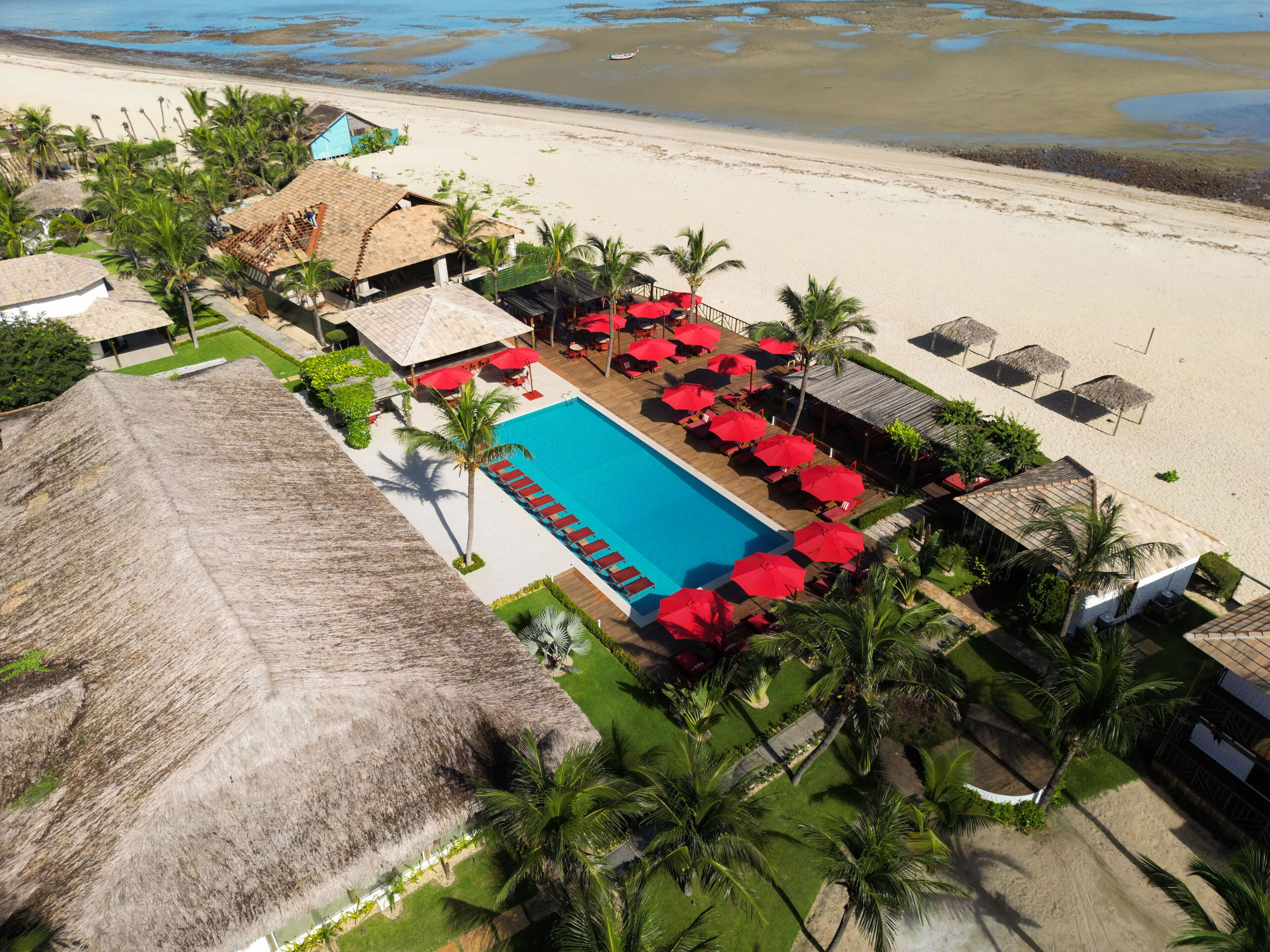 A resort with a swimming pool, beach, and thatched-roof structures.