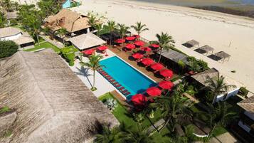 A resort with a swimming pool, beach, and thatched-roof structures.