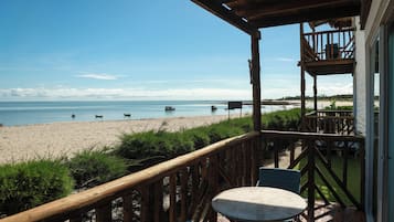 A wooden deck with a table and chairs overlooking a beach with boats and a clear sky.