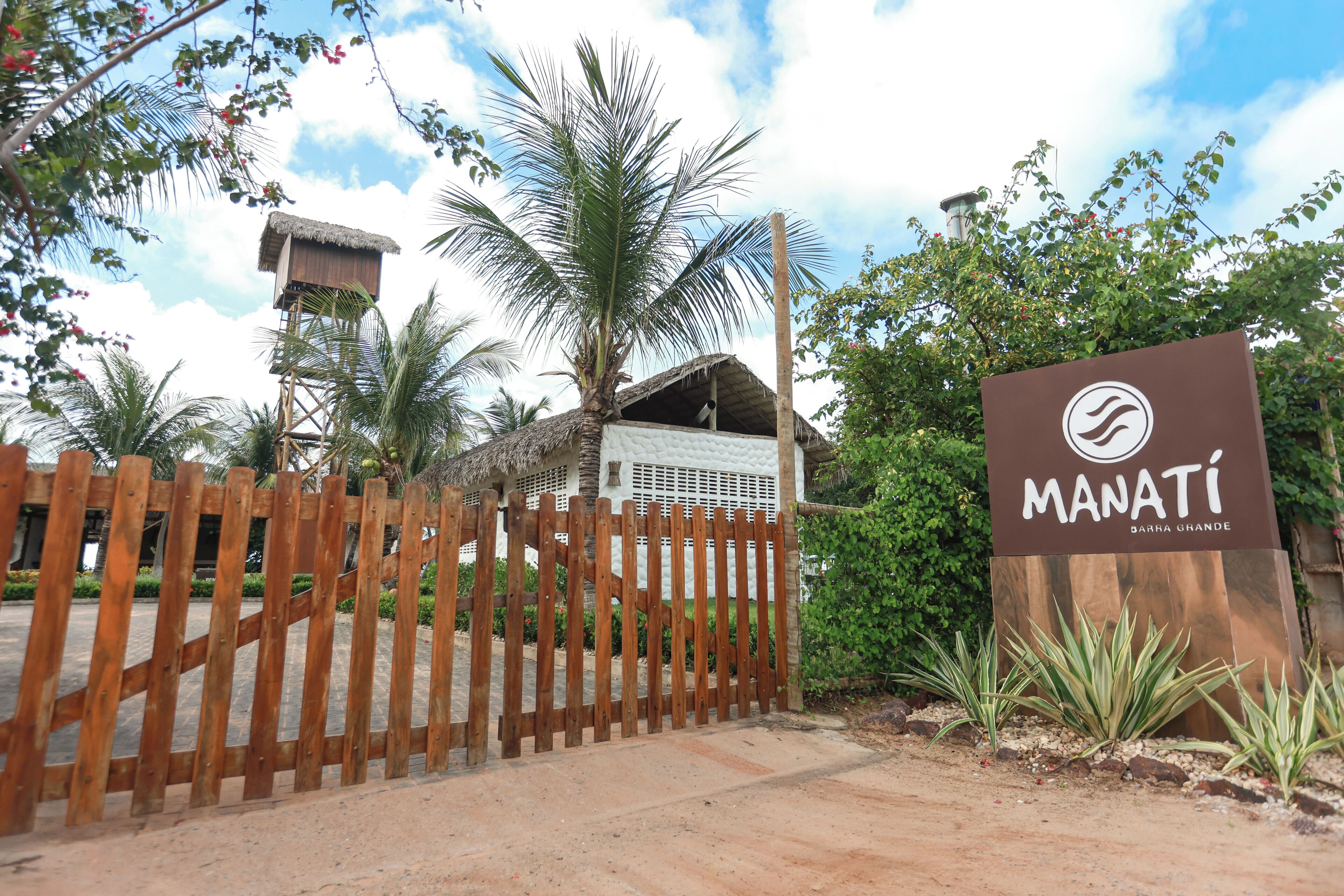 A wooden fence, a sign for Manati, and a building with a thatched roof.