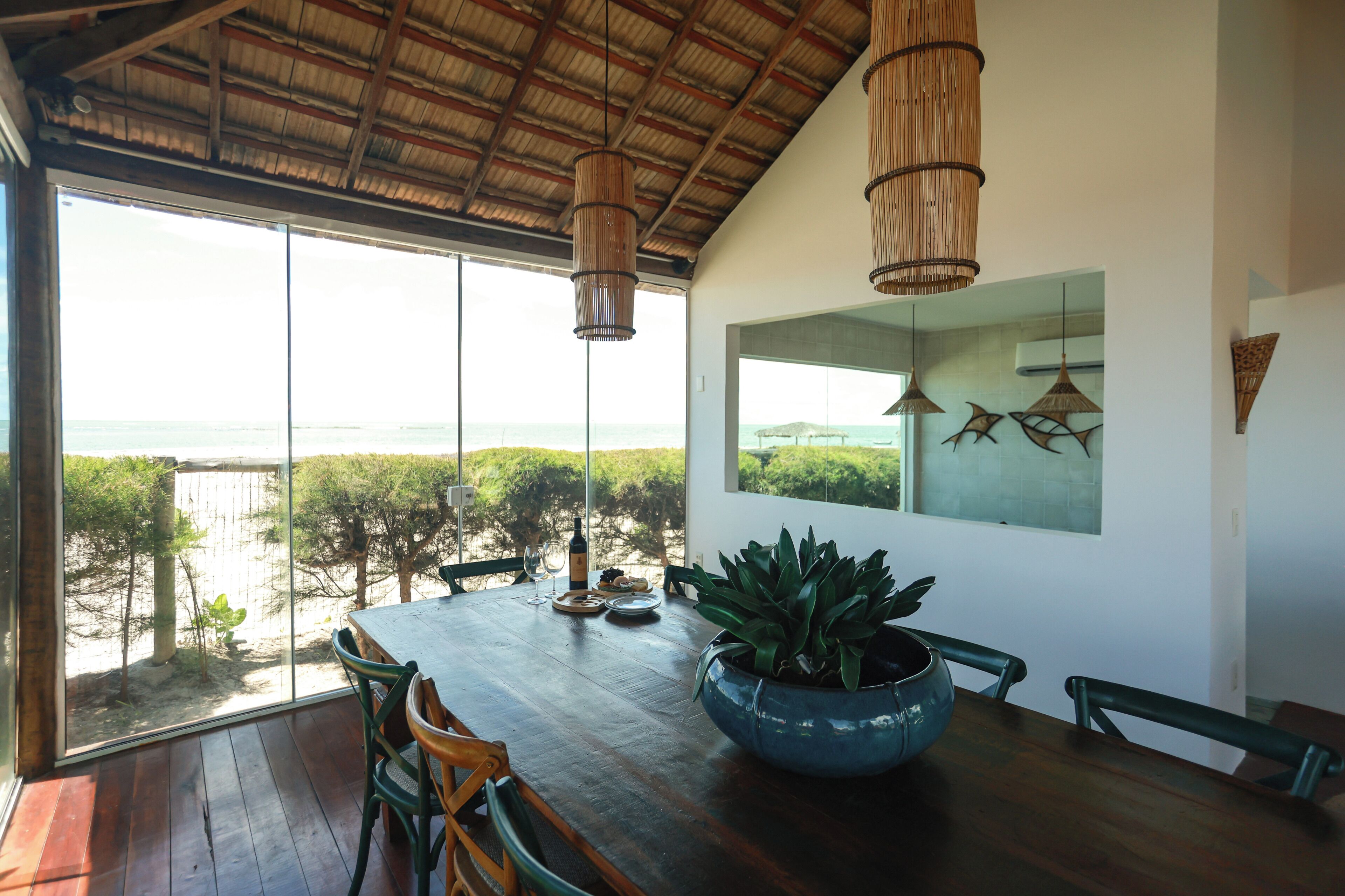 A dining area with a large table, chairs, a potted plant, and a view of the ocean.