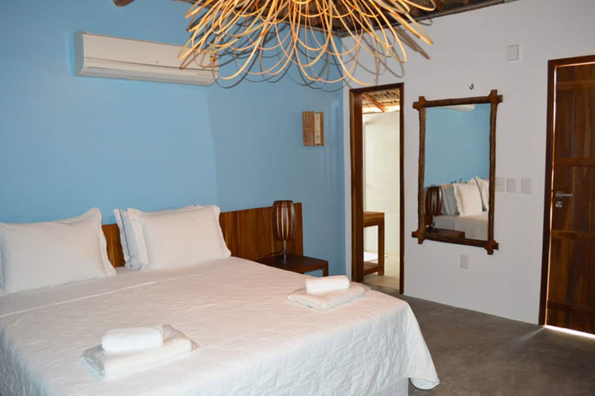 A bedroom with a large bed, a wooden nightstand, a mirror, and a door leading to another room.