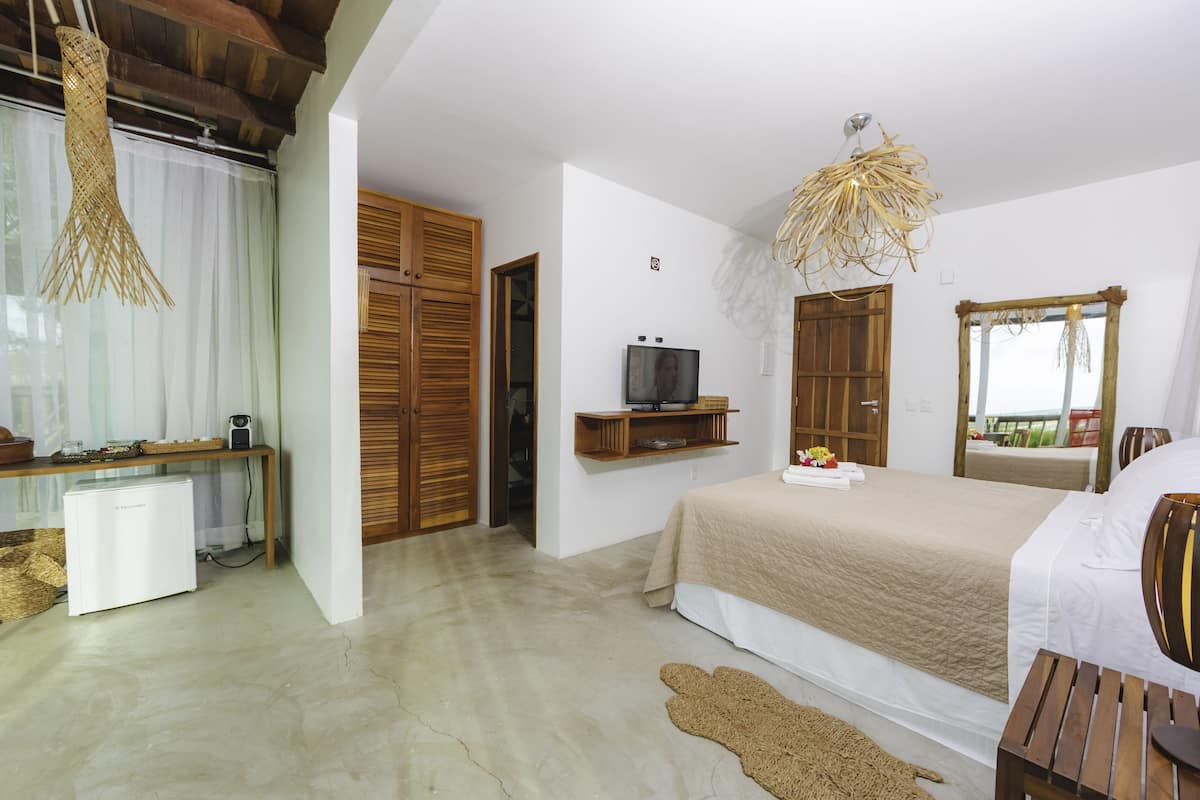 A bedroom with a bed, a television, a wooden wardrobe, a small table, and a hanging light fixture.