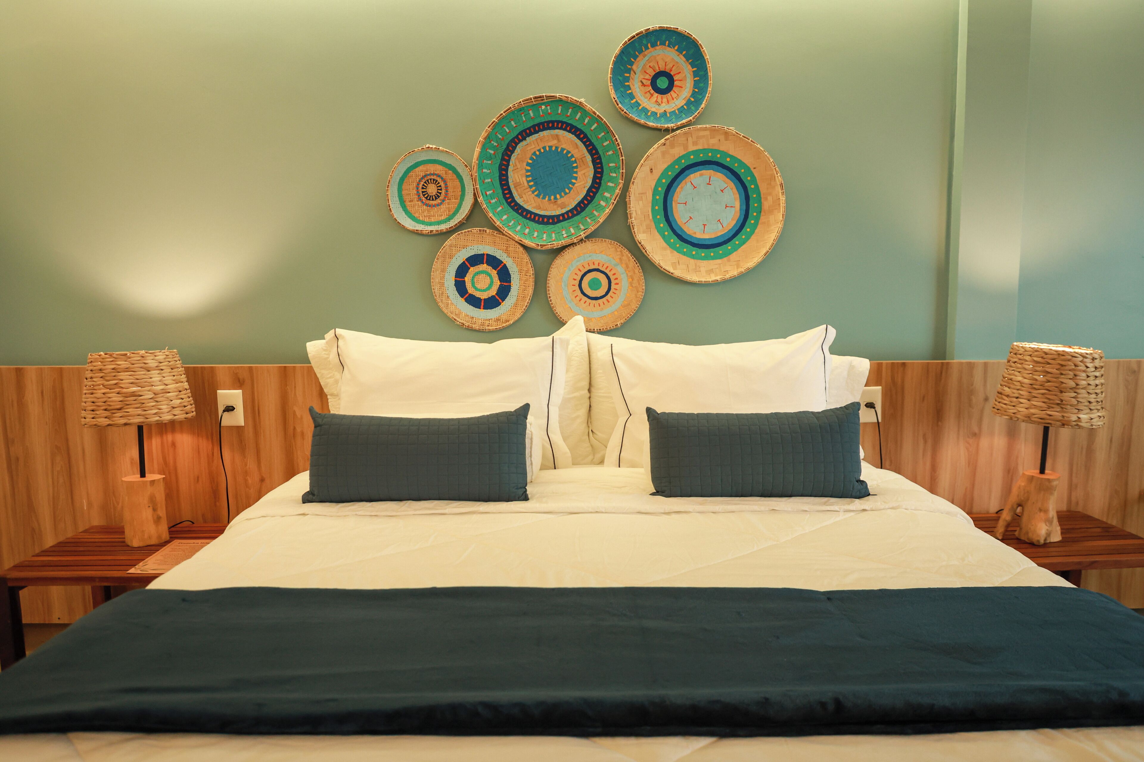 Una cama con una colcha blanco y verde oscuro, dos almohadas y un cabecero con un adorno circular en la pared.