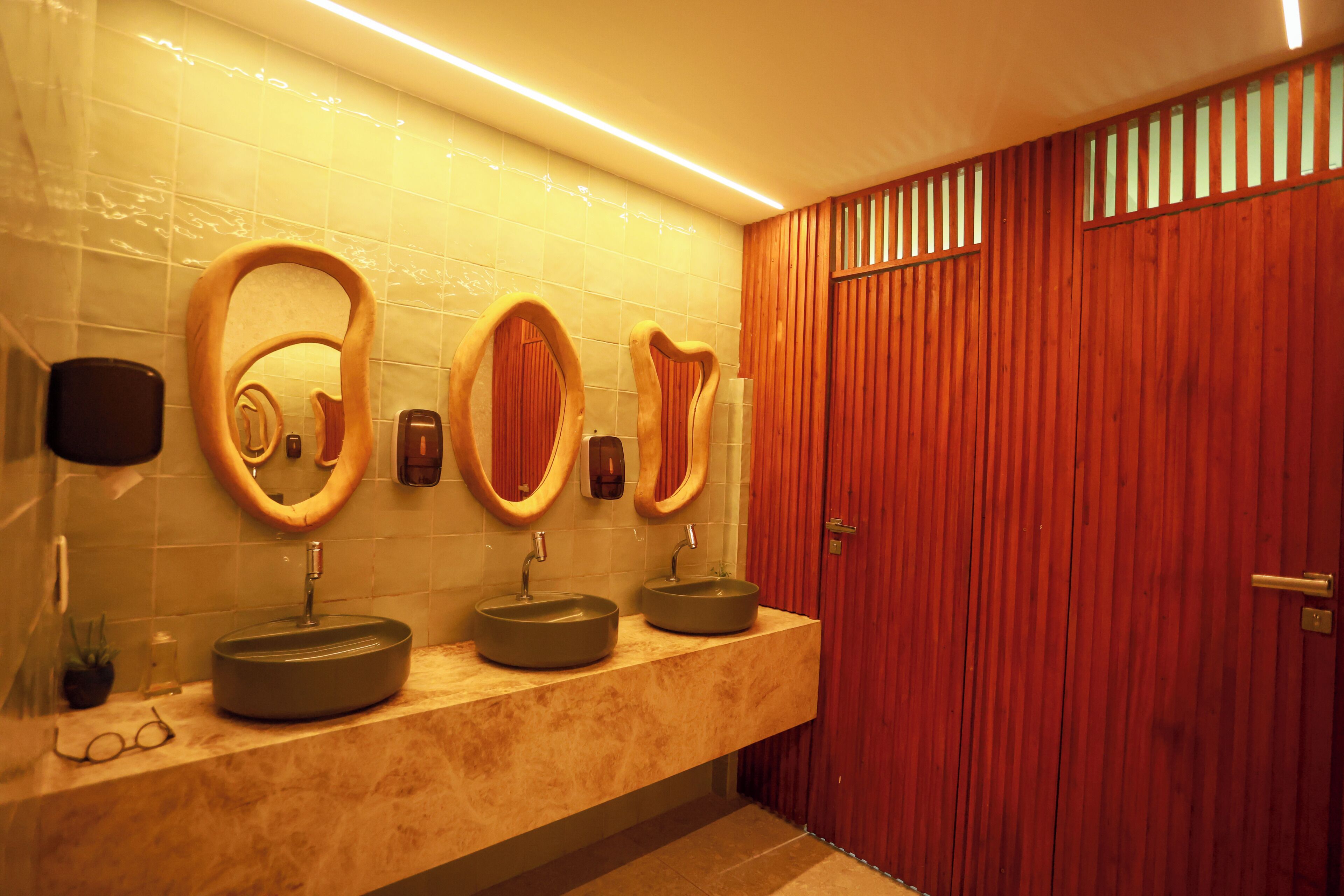 A bathroom with a marble countertop, three sinks, and wooden-framed mirrors.