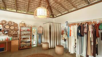 A boutique with a rustic interior, featuring a clothing rack, shelves with various items, and a woven ceiling.